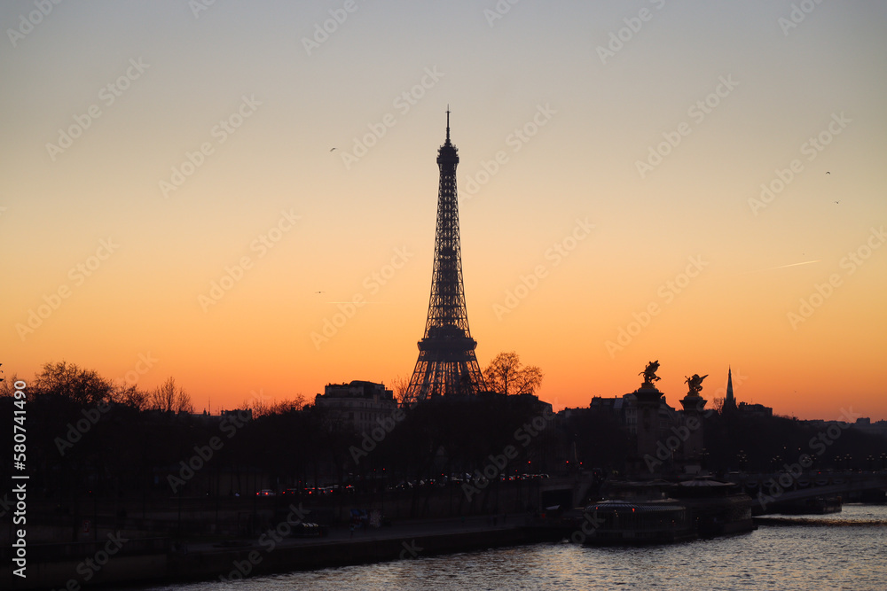A silhouette of Eiffel tower at sunset with Seine river surround with building and urban scenic of Paris with orange sky in the evening 