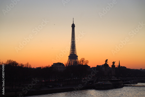 A silhouette of Eiffel tower at sunset with Seine river surround with building and urban scenic of Paris with orange sky in the evening 