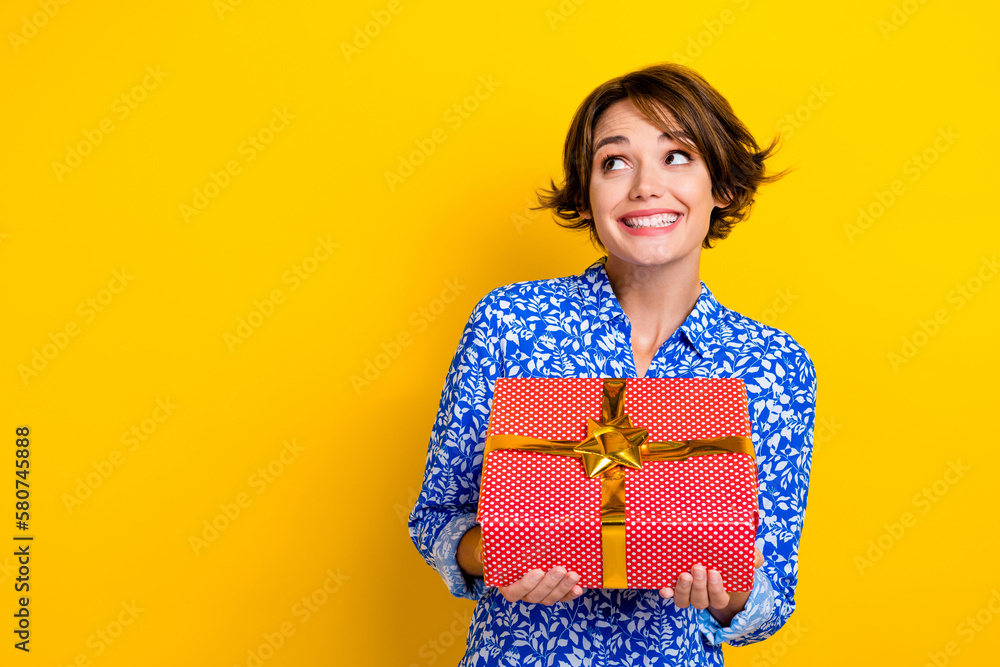 Photo of funky dreamy lady wear print shirt getting red gift package looking empty space isolated yellow color background Photo of funky dreamy lady wear print shirt getting red gift package looking empty space isolated yellow color background