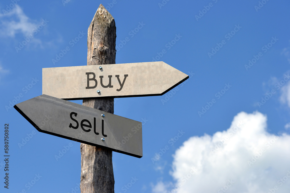 Buy or sell - wooden signpost with two arrows, sky with clouds Buy or sell - wooden signpost with two arrows, sky with clouds