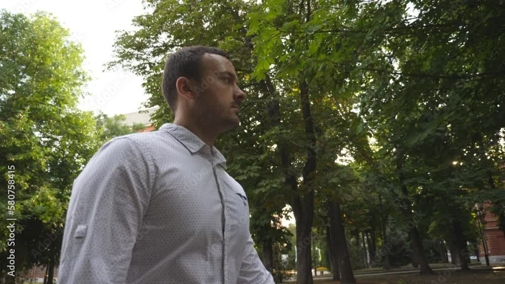 Young successful businessman looking on his phone during walking in city park. Confident entrepreneur checking time while going at business deal. Executive office worker on his way to job. Slow motion Young successful businessman looking on his phone during walking in city park. Confident entrepreneur checking time while going at business deal. Executive office worker on his way to job. Slow motion