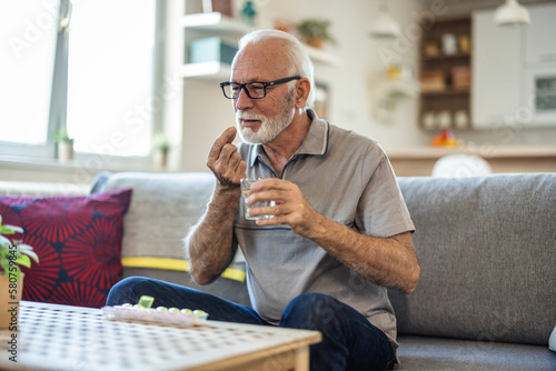 Senior man takes pill with glass of water in hand. Stressed mature man drinking sedated antidepressant meds. Man feels depressed, taking drugs. photo