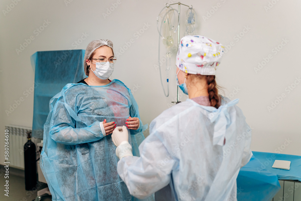 Nurse ties a sterile gown to the surgeon before the operation. Doctors