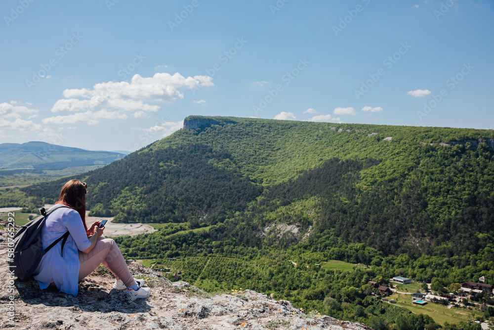 a woman sitting with a phone on a mountain hiking journey nature