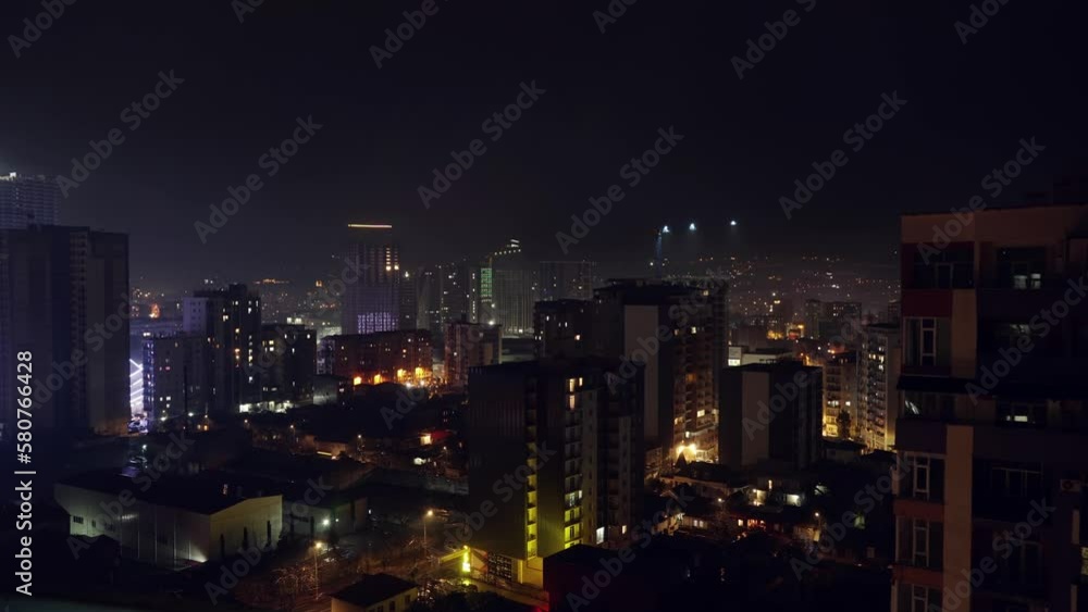 Frame-by-frame night cityscape and high-rise buildings in center of metropolis . Batumi in Georgia with panoramic views. Cloud flies over houses. Business district against backdrop of mountains. Frame-by-frame night cityscape and high-rise buildings in center of metropolis . Batumi in Georgia with panoramic views. Cloud flies over houses. Business district against backdrop of mountains.