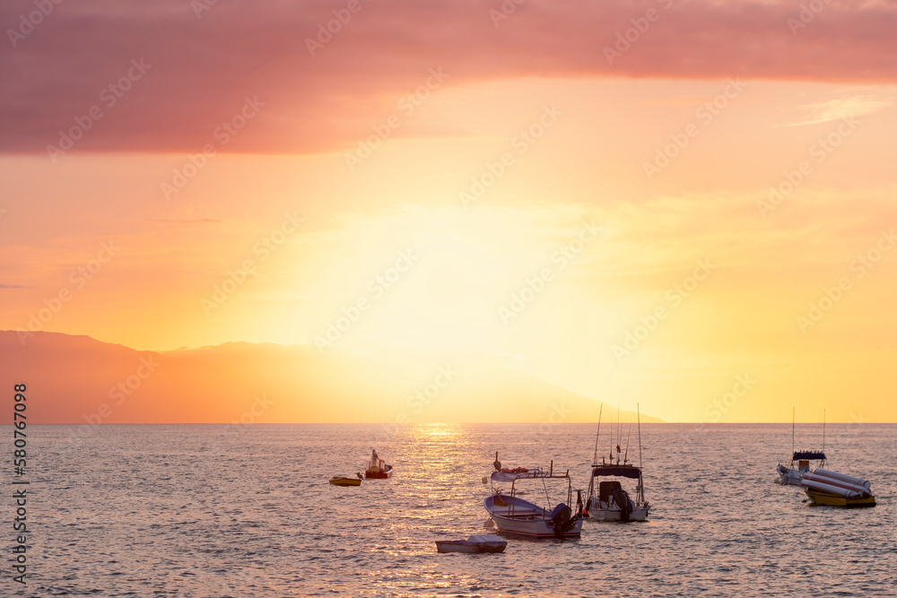 Silhouettes of sail and fishing boats in the ocean marina at sunset hour, selective focus, beautiful colorful orange sky. Water sports, travel, tourism concept.