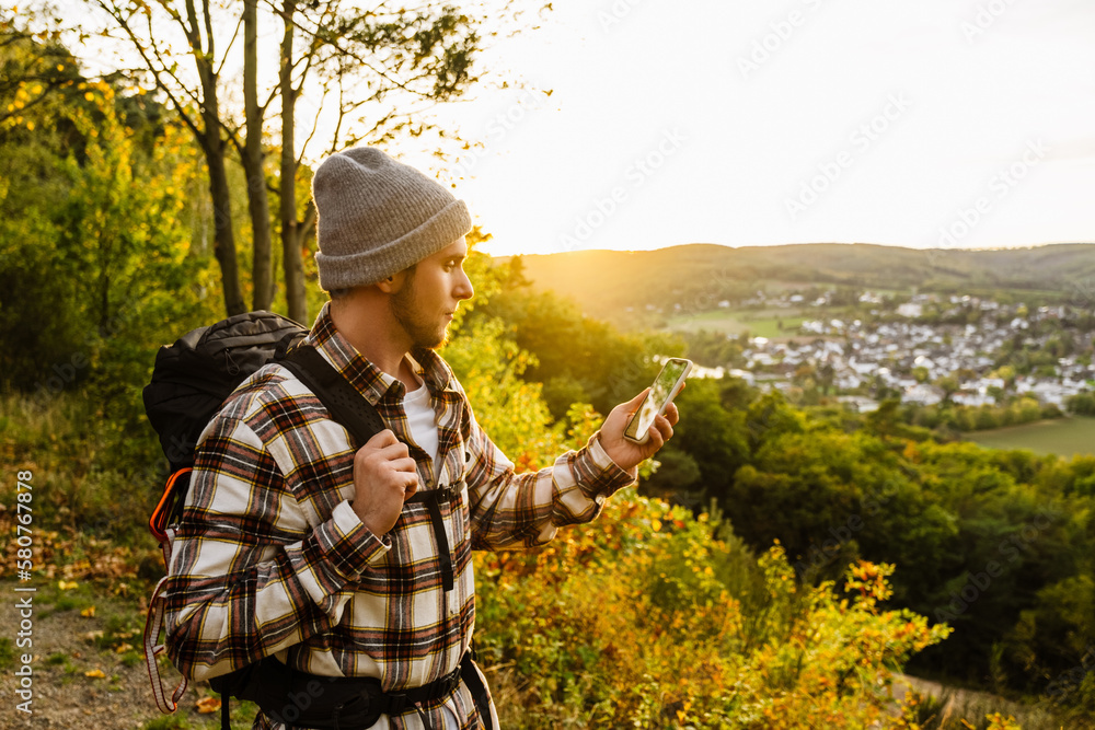 Young man tourist using mobile phone while standing at forest glade