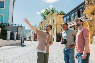 tour guide in sunglasses pointing with hand during excursion with interracial tourists on Andrews descent in Kyiv.