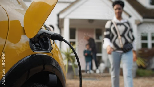 Woman walking up to unplug electric car charging on driveway outside house