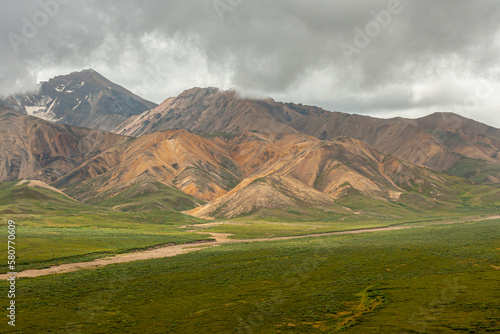 Denali Park, Alaska, USA - July 25, 2011: Confluence of 2 semi-dry rivers on green tundra. Thick gray cloudscape over dark-brown and pale-brown mountains