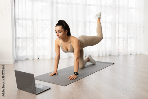 Athletic young woman doing pilates at home, watching fitness video