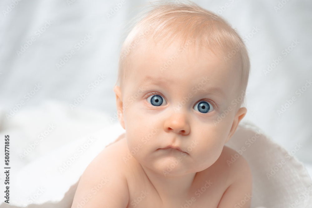 Cute baby with blue eyes - closeup portrait. Little boy looking at camera. Child lying on bed covered by bath towel. Cute baby with blue eyes - closeup portrait. Little boy looking at camera. Child lying on bed covered by bath towel.