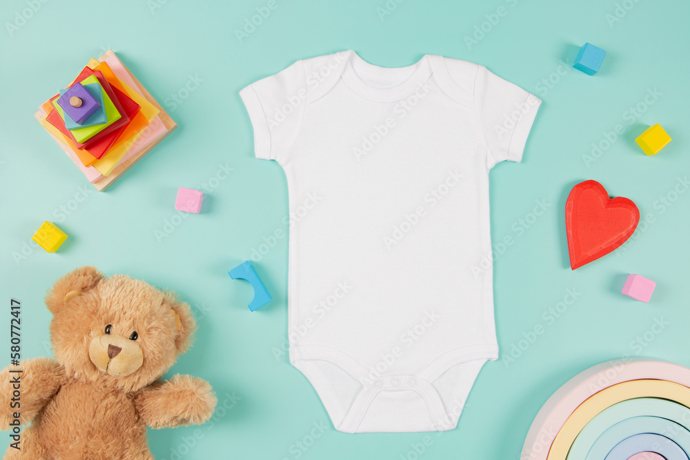 White cotton baby short sleeve bodysuit, teddy bear and natural wooden eco-friendly toys on pastel background. Infant onesie mockup. Blank gender neutral newborn bodysuit template mock up. Top view - obrazy, fototapety, plakaty 
