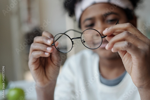 Selective focus on hands of African American boy holding eyeglasses with round frame while having break after preparing homework
