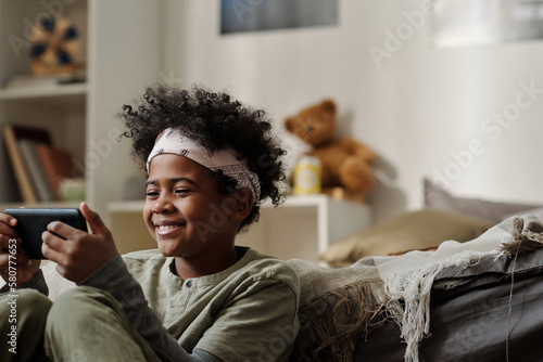 Canvastavla Smiling African American boy in headband looking at smartphone screen while comm
