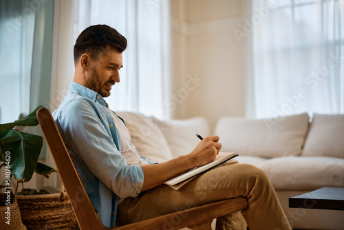 Smiling man writes in notebook while relaxing at home.