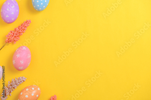 Happy Easter holiday greeting card design concept. Colorful Easter Eggs and spring flowers on yellow background. Flat lay, top view, copy space.