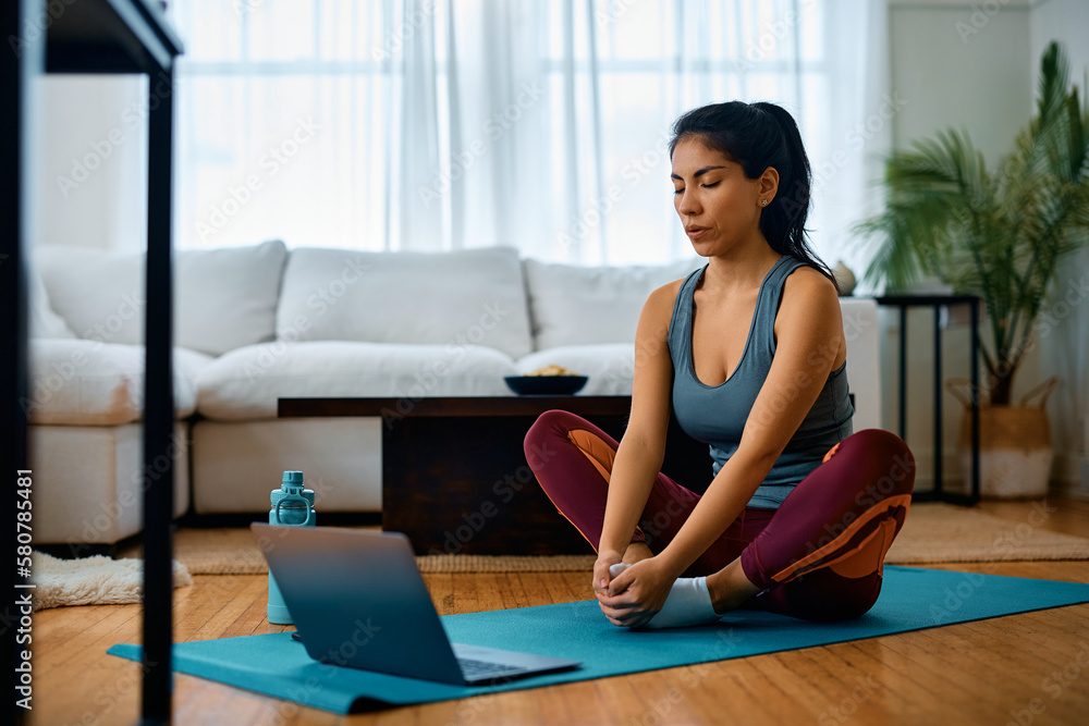 Athletic woman working out at home while following online exercise class on laptop. Athletic woman working out at home while following online exercise class on laptop.