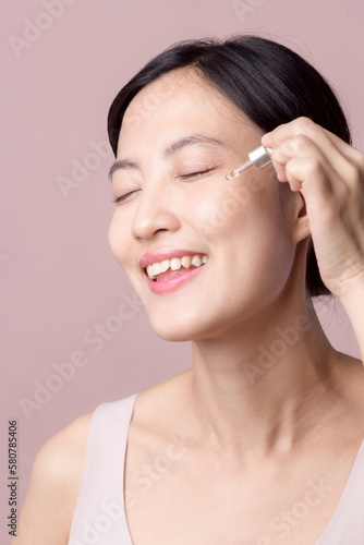 Beautiful young asian woman applying serum facial oil on natural mack up face skin. Portrait health wellness clean skincare female attractive person with treatment dropper. Beauty  cosmetology concept
