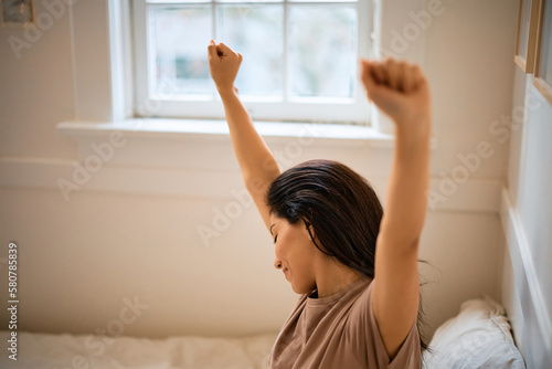 Smiling woman stretching while waking up in her bedroom.