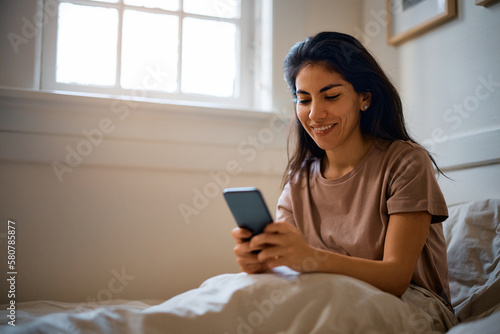 Happy woman text messaging on cell phone in bedroom.