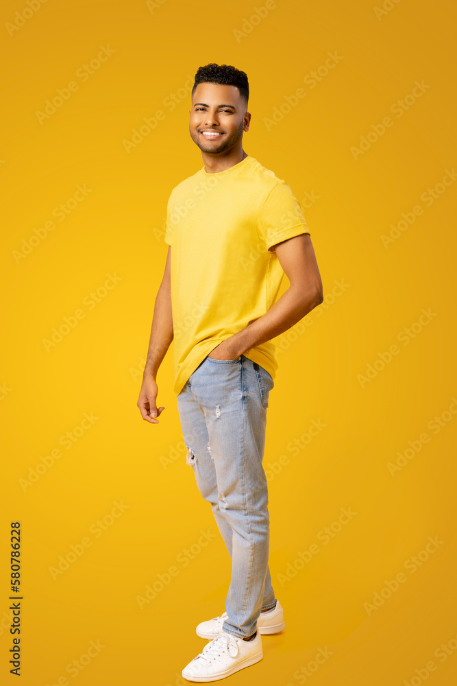 Portrait of happy satisfied Indian young man in t-shirt standing and looking at the camera with light smile isolated on yellow. Indoor studio shot of handsome guy in full length Portrait of happy satisfied Indian young man in t-shirt standing and looking at the camera with light smile isolated on yellow. Indoor studio shot of handsome guy in full length