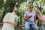 overjoyed multiethnic friends with beer talking while spending time in park.