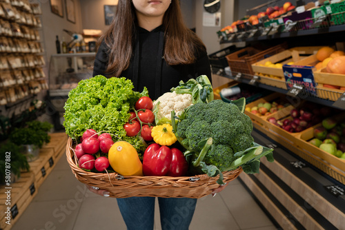 a young girl with a wooden basket full of fresh vegetables in her hands stands in a store