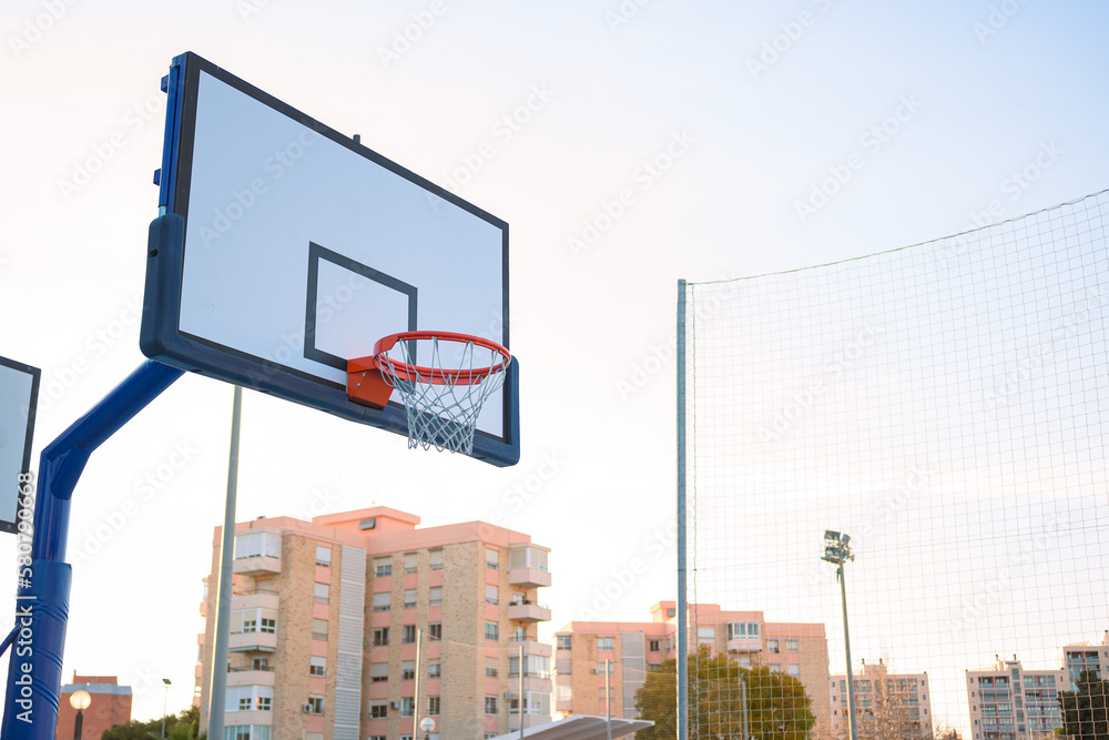 A basket on a street basketball court at sunset