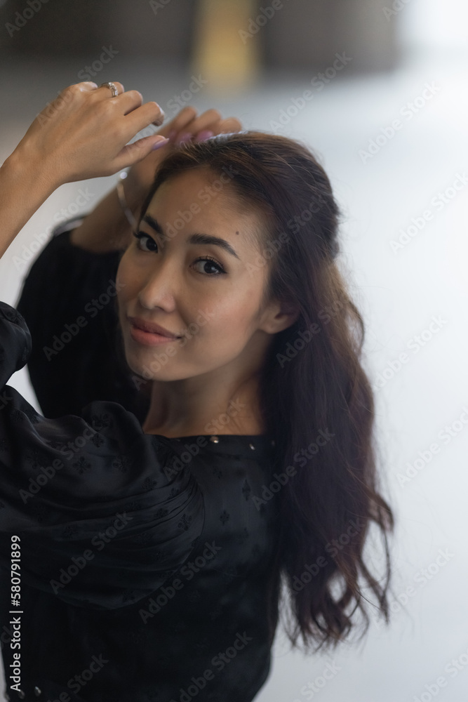 Fototapeta premium A beautiful Asian girl with black hair in a white dress against a yellow wall. Feminine attractiveness. A person with an aesthetically pleasing facial structure. A model for makeup and hairstyle
