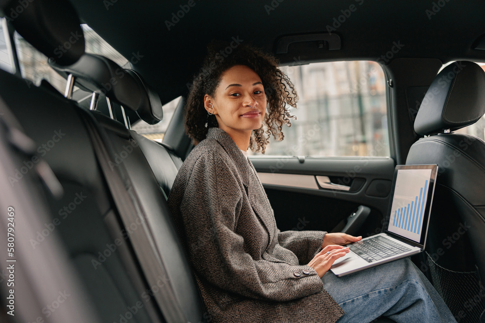 Smiling businesswoman analyst working on laptop sitting car leather backseat on way to office