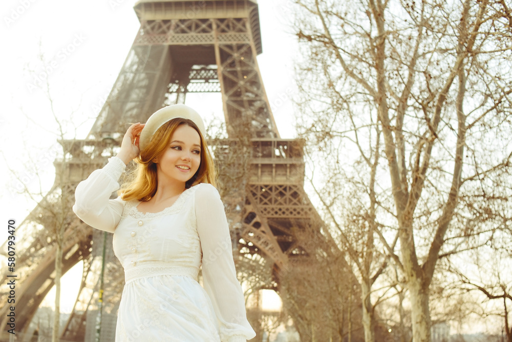 A girl against the backdrop of the Eiffel Tower in Paris in a beret and a dress with curled hair, a romantic journey. Woman laughing and looking away.