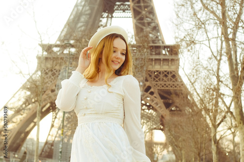 A girl against the backdrop of the Eiffel Tower in Paris in a beret and a dress with curled hair, a romantic journey. Woman laughing and looking away.