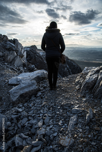 A woman stands with her back on the edge of the cliff. Rocky mountain at sunset.