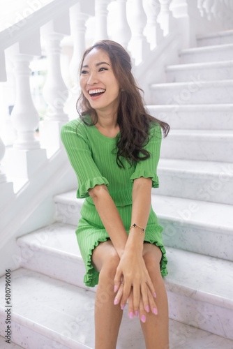 An elegant and beautiful Asian model in a green dress strikes a pose that's both graceful and captivating. Her dark hair, beautiful lips, and attractive facial features make for an alluring image 