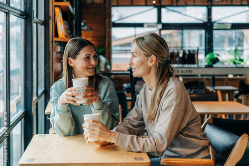 Two women sitting in a coffee house talking and drinking coffee.
