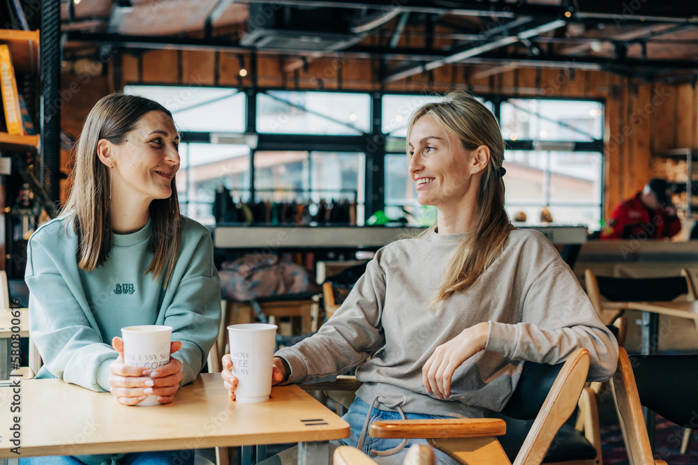 Two smiling happy female friends sitting in a coffee house, chatting and drinking coffee. Two smiling happy female friends sitting in a coffee house, chatting and drinking coffee.