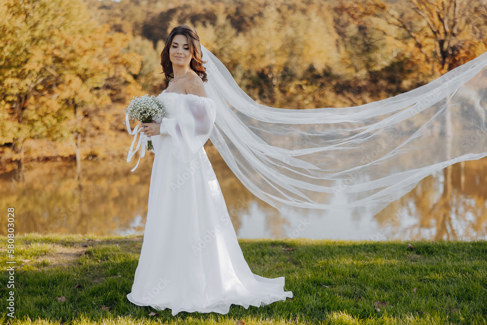 Portrait of a beautiful young bride in an elegant white dress with a long veil and a bouquet of gypsophila near the lake in soft light. Portrait of a beautiful young bride in an elegant white dress with a long veil and a bouquet of gypsophila near the lake in soft light.