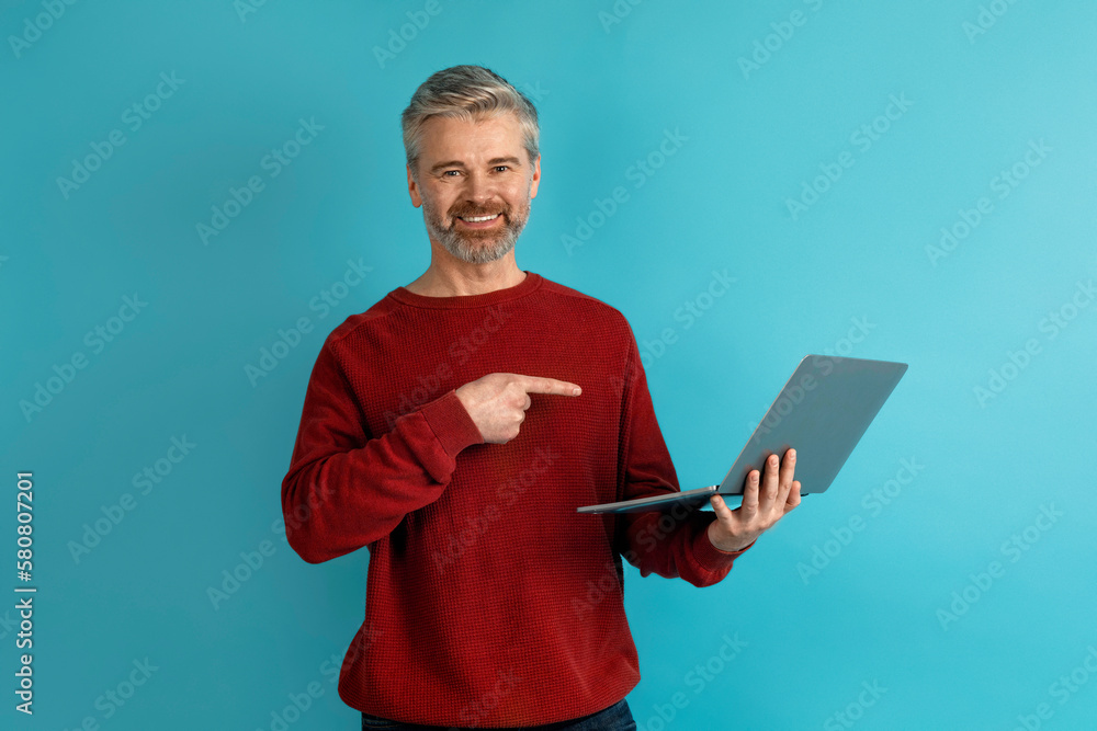 Positive middle aged man using laptop on blue Positive middle aged man using laptop on blue