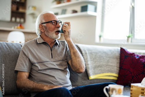 Senior man inhaling asthmatic cure at home. Man is living life with chronic illness everyday and overcoming challenges with It. Older man having an asthma attack due to his allergies.