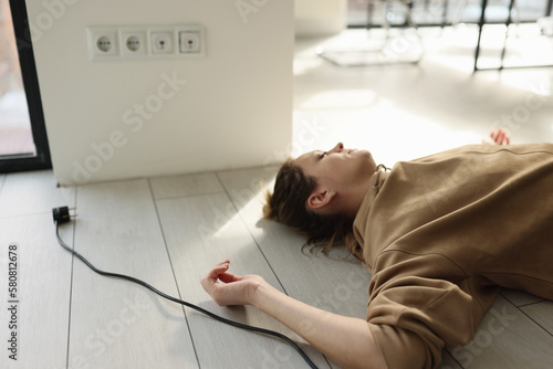 Foto Woman lies on the floor with her eyes closed near electric cable with plug