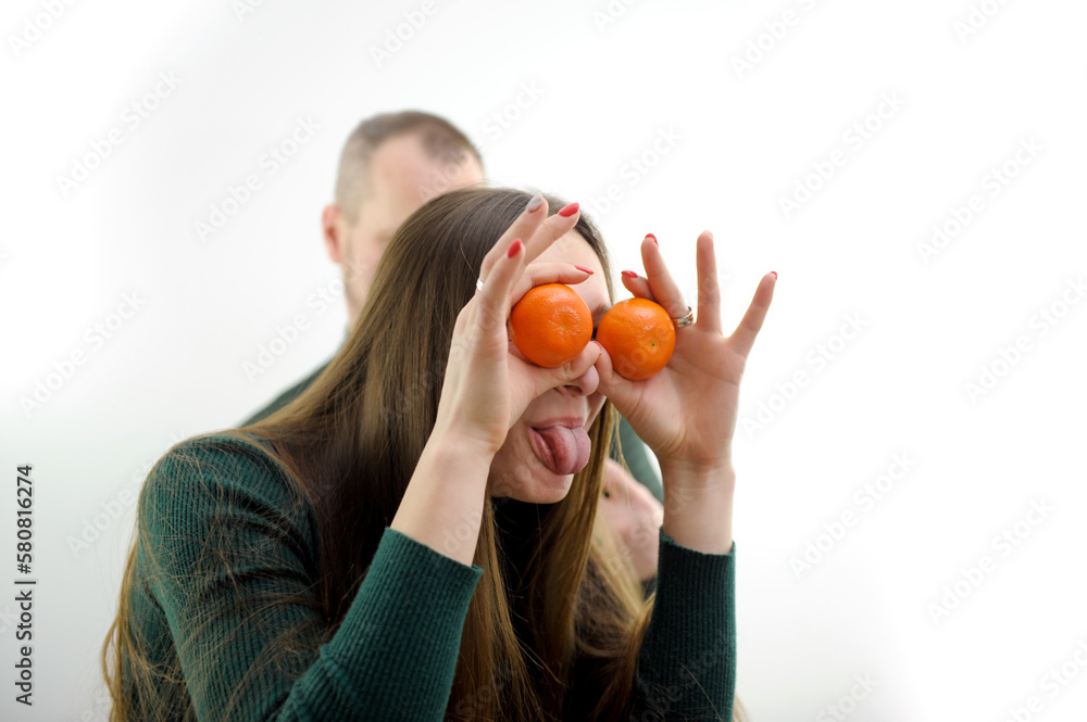 young girl put Tangerines to eyes and pulled out tongue stuck out and she twists and makes faces in the background a man on a white background green sweater long hair joke fooling around grimacing young girl put Tangerines to eyes and pulled out tongue stuck out and she twists and makes faces in the background a man on a white background green sweater long hair joke fooling around grimacing