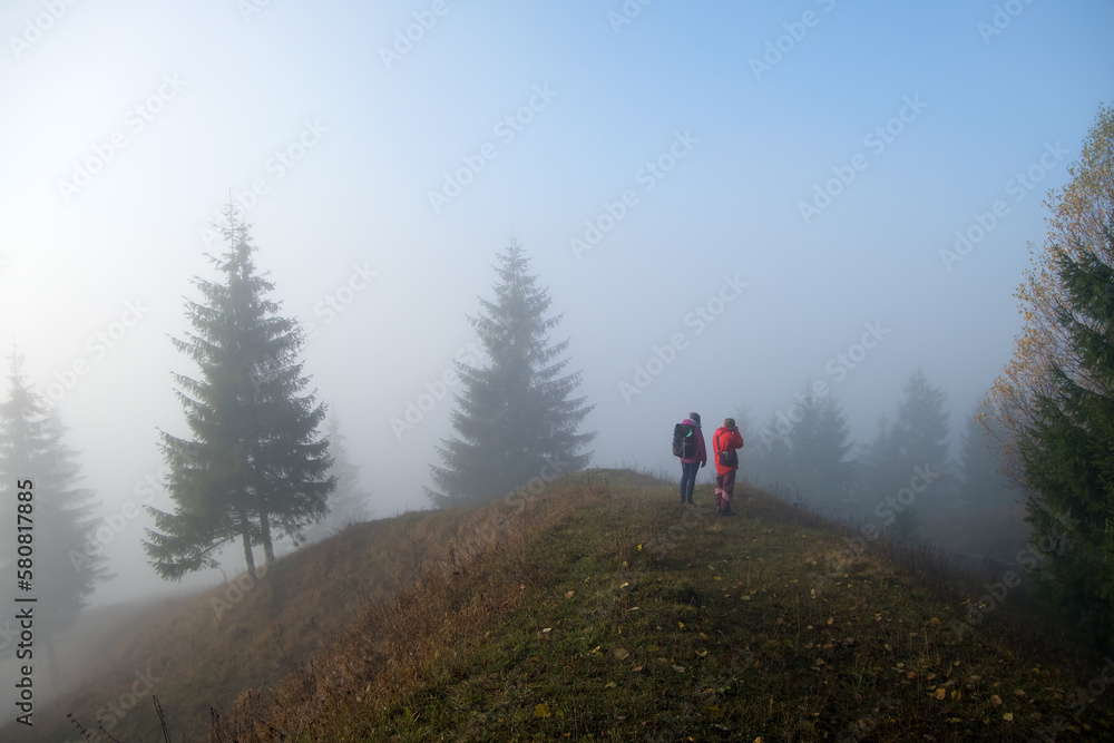 Small figure of lonely hikers enjoying his time on wild forest trail on foggy autumn day