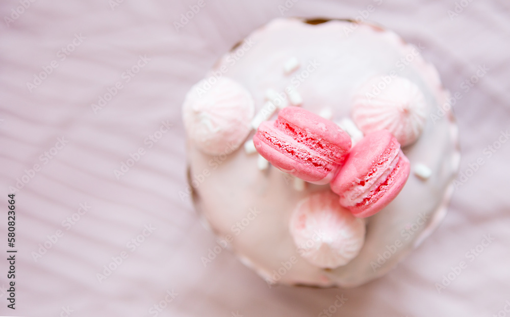 A traditional paska decorated with pink swiss chocolate and meringue stands on a pink tablecloth. Easter holiday, top view. Place for writing. A traditional paska decorated with pink swiss chocolate and meringue stands on a pink tablecloth. Easter holiday, top view. Place for writing.