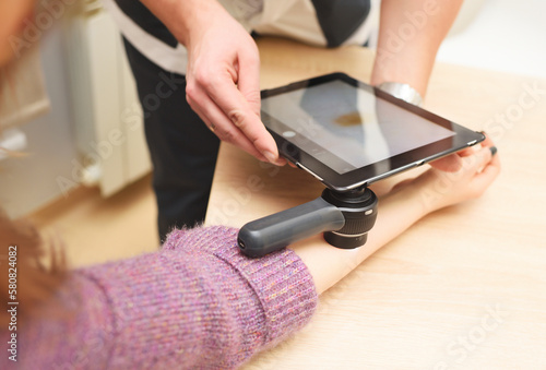 dermatologist examines moles on a female patient's arm with a dermatoscope and a computer tablet. Prevention of melanoma. photo