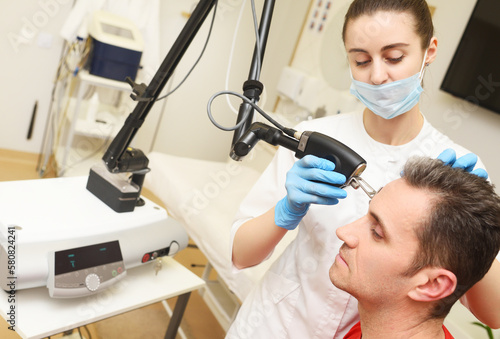 cosmetologist uses a CO2 fractional ablative laser to rejuvenate the skin of the face and remove vascular asterisks from a male patient in a modern cosmetic beauty clinic. photo