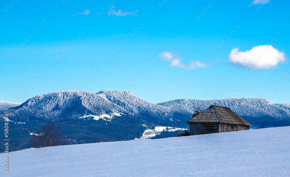 Landscape with an old wooden hut on a snowy field in the mountains