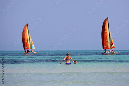 Two women in swimwear in water on tropical beach on sailboats background. Sunny coast with swimming people in Atlantic ocean