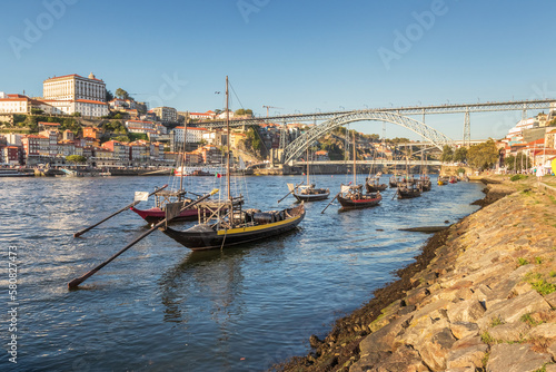 Rabelo boats moored on the Douro River, with the city of Porto and the D. Luís bridge in the background, on a summer afternoon.