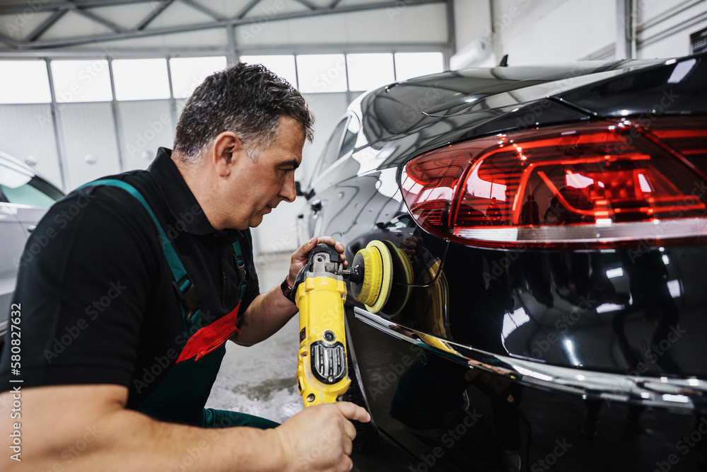 Fototapeta premium Professional car service worker polishing luxury car with orbital polisher in a car detailing and valeting shop. Ultra wide angle shot.